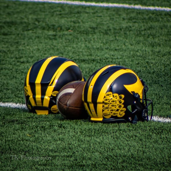 two Michigan football helmets with a football between them