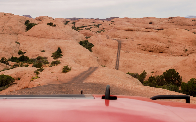 jeep driving a trail across slickrock in moab utah