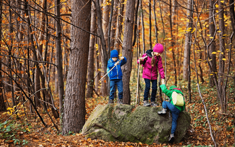 three kids climbing a large rock while hiking