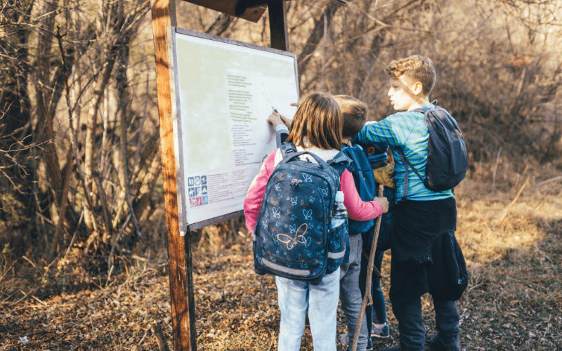 three kids reading a hiking trailhead information sign